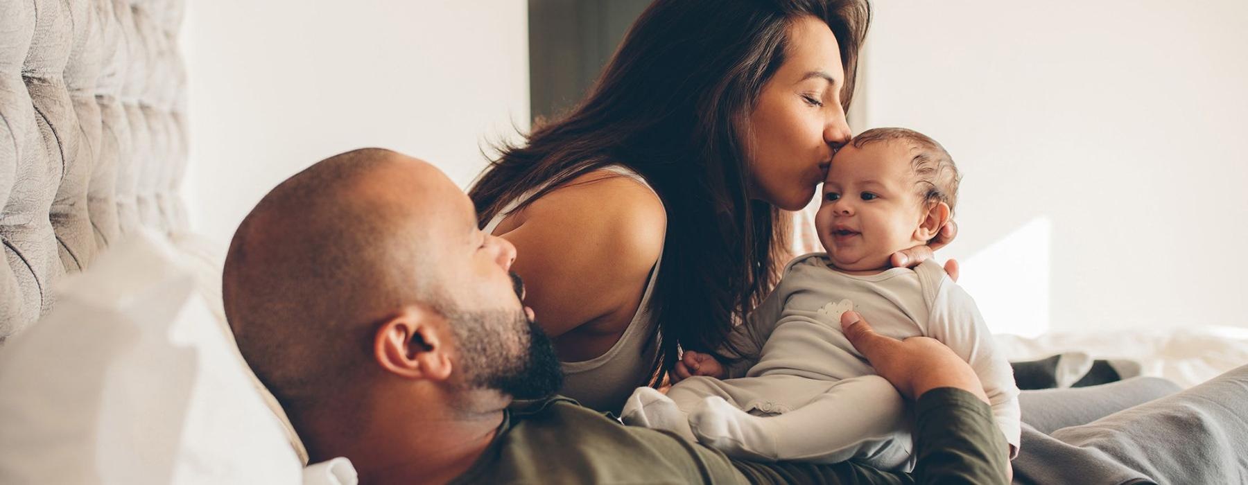 A perfect fit for the whole family mother kisses her infant while father lies in bed and holds him